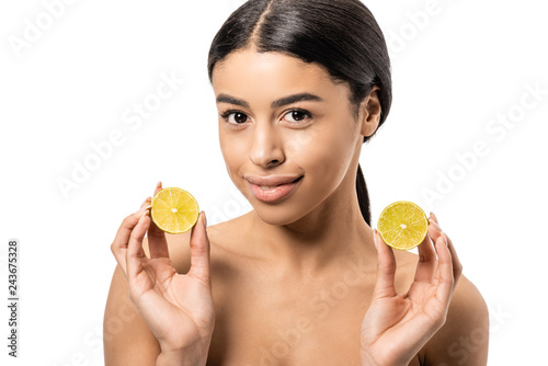 attractive naked african american girl holding halves of lime and smiling at camera isolated on white