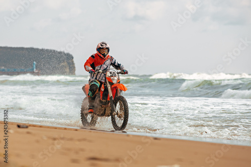 Motorcyclist in a protective suit rides a motorcycle on the sea, splashes fly from under the wheels.