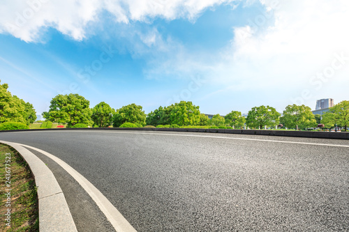 Urban asphalt road and green trees under blue sky