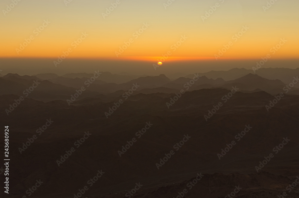 Scenic sunrise in the mountains. The sun comes out from the cloud. View from Mount Sinai (Mount Horeb, Gabal Musa, Moses Mount). Sinai Peninsula of Egypt