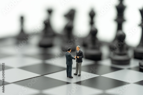 Miniature 2 people businessmen Shake hands on a chessboard with a chess piece on the back Negotiating in business. as background business concept and strategy concept with copy space.