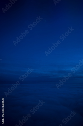 Night sky of dark blue color and strong clouds and very small moon silhouette