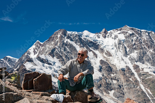 A mountaineer smiles satisfied with the climb, in the background the peaks of the imposing east face of Monte Rosa above Macugnaga in Piedmont, Italy.
