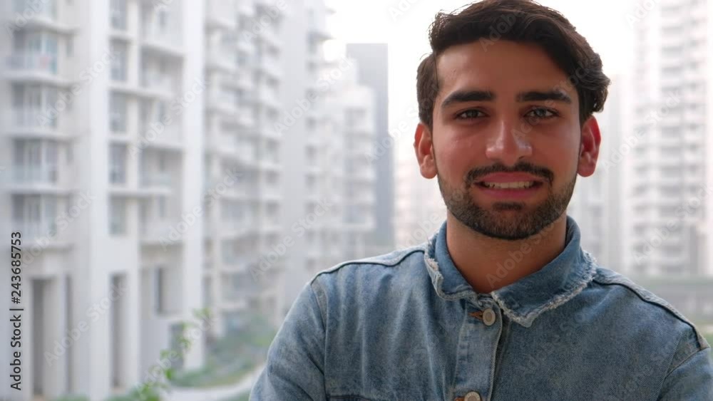 Handheld stabilized man turns around looks at camera as he smiles with his building complex facade in the background Handheld stabilized man turns around looks at camera as he smiles with his building complex facade in the background