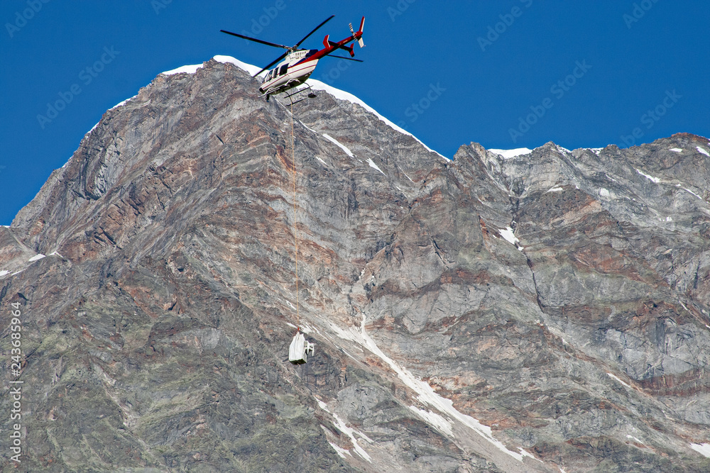 A helicopter transports material in the high mountains.