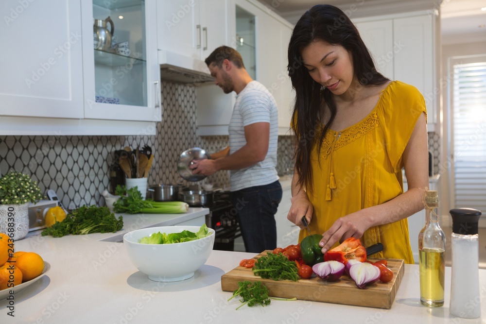 Woman cutting vegetables while man cooking food in kitchen