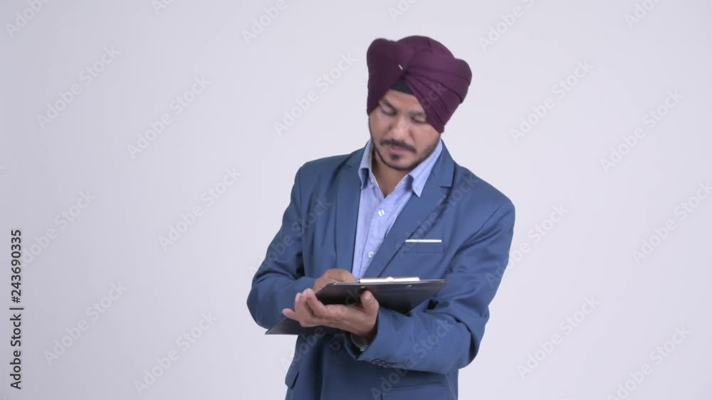 Bearded Indian Sikh businessman talking while reading on clipboard Bearded Indian Sikh businessman talking while reading on clipboard