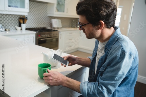 Man using mobile phone while having coffee in kitchen