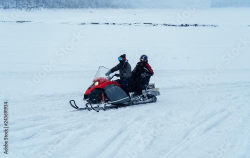 Two man on a snowmobile riding on the snow surface in the mountains.