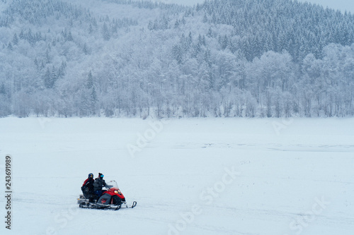 Two man riding fast on a snowmobile in the snowy mountains near the forest