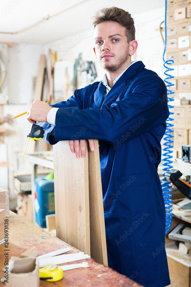 Young smiling woodworker taking measurements