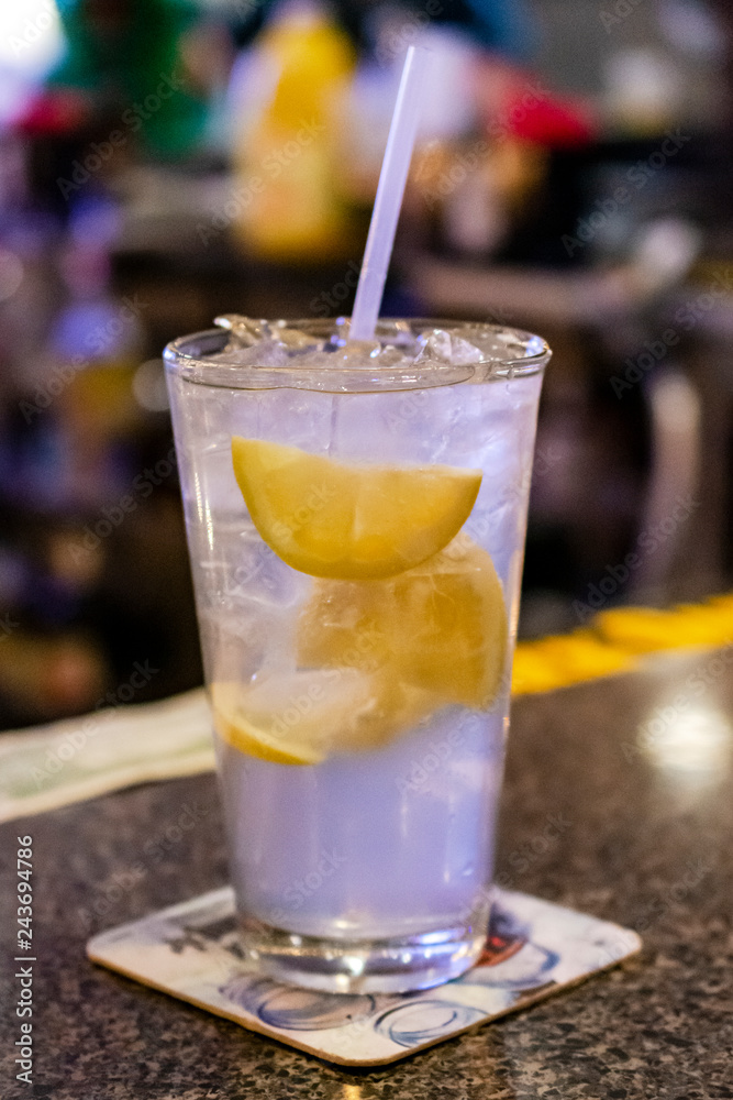 Alcohol drink on bar with lemon slices and a straw.  Blurred background.