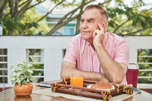 Pensive senior man sitting in outdoor cafe with tray with breakfast in front of him