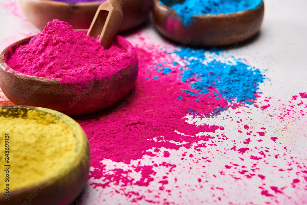 wooden spatula and bowls with pink, blue and yellow holi powder on white background wooden spatula and bowls with pink, blue and yellow holi powder on white background