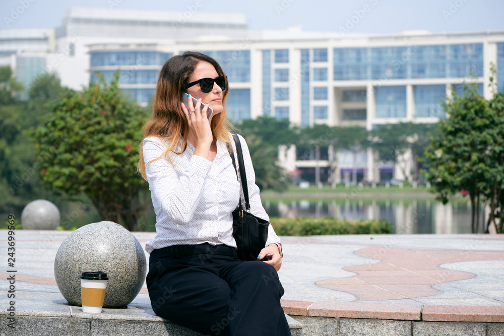 Elegant feminine business lady sitting outdoors and talking on phone