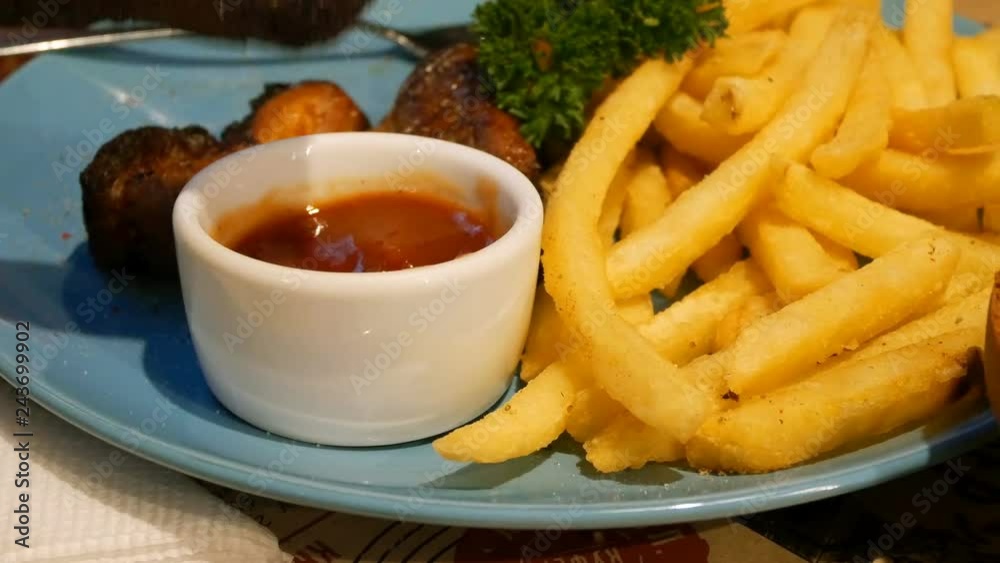 Tasty dinner with grilled pork ribs, french fries and ketchup. Fried appetizing pork ribs are dipped in ketchup and eat in a restaurant or cafe. Tasty dinner with grilled pork ribs, french fries and ketchup. Fried appetizing pork ribs are dipped in ketchup and eat in a restaurant or cafe.