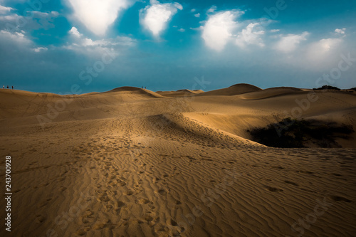 Light and shadow at the night in sand yellow desert with blue sky and white clouds in background for amazing landscape concept for wild holiday or wanerlust lifestyle - people lot of footprints