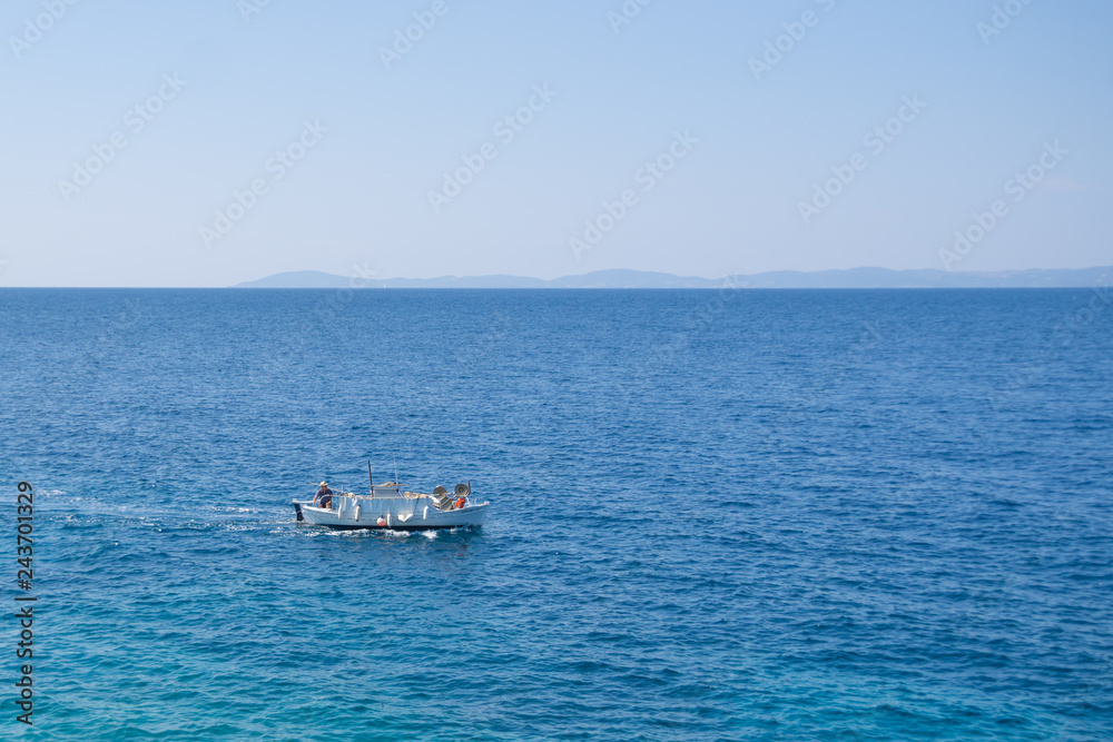 Small white motorized boat with one man sails in the open sea Small white motorized boat with one man sails in the open sea
