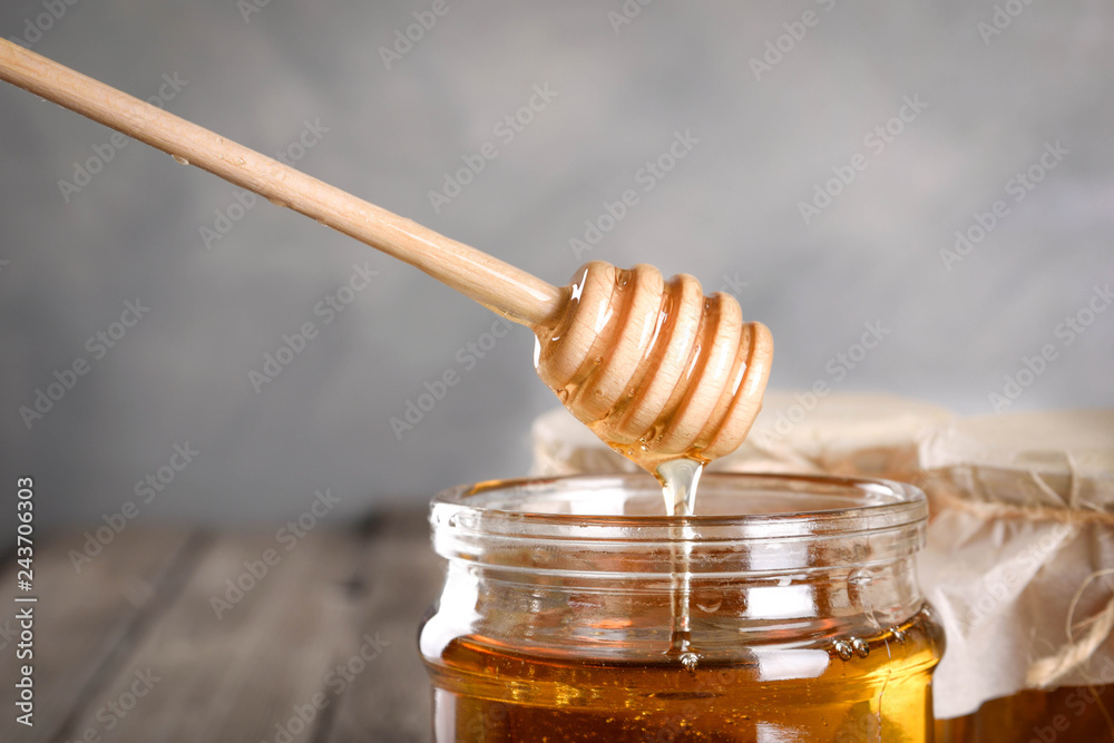 Pouring aromatic honey into jar, closeup. Honey in glass jars and honeycombs wax on wooden background. Wooden stick , instruments Pouring aromatic honey into jar, closeup. Honey in glass jars and honeycombs wax on wooden background. Wooden stick , instruments