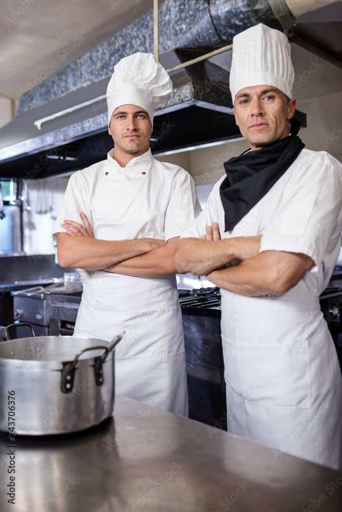 Two male chefs standing with arms crossed in kitchen