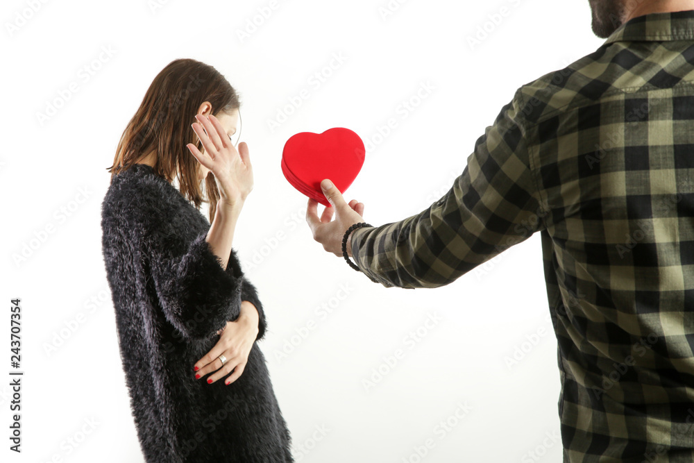 Portrait of a young couple having conflict. Man asking for forgiveness offering a red heart-shaped gift to his depressed girlfriend Portrait of a young couple having conflict. Man asking for forgiveness offering a red heart-shaped gift to his depressed girlfriend