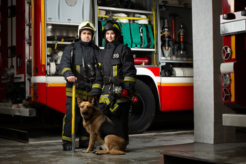 Photo of man, woman and dog firefighter near fire truck