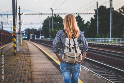 Woman with backpack is looking at arriving train at a railway station early morning