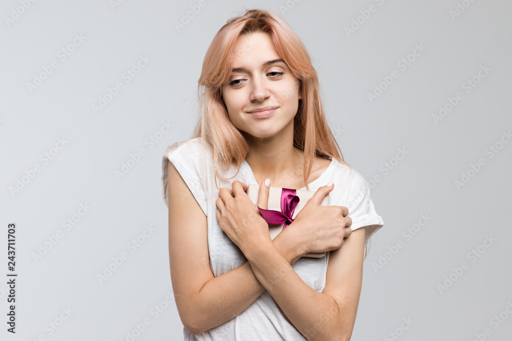 Studio portrait of cute blonde teen in white t-shirt presses the gift to the chest and attached to memories/received a gift on Valentine's Day/pleasant surprise, gift in box, joyful glee, lovers day. Studio portrait of cute blonde teen in white t-shirt presses the gift to the chest and attached to memories/received a gift on Valentine's Day/pleasant surprise, gift in box, joyful glee, lovers day.