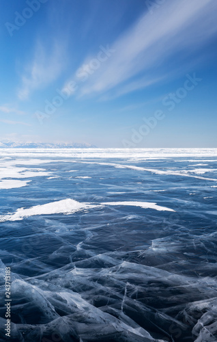 Winter landscape of the frozen Lake Baikal on a cold February day. Transparent beautiful ice with cracks against the blue sky with stratus clouds. Natural background