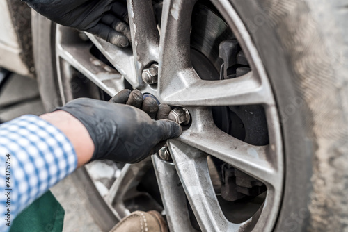 Hands in gloves fixing nuts on car wheel closeup