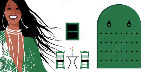 Woman with long brown hair and large earrings, on background of typical Spanish Mediterranean style village. Green door and window, chairs and small table with vase on white walls. photo
