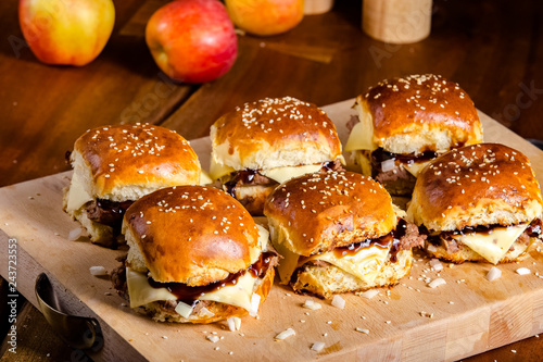 The process of making burgers with meat, bacon, fresh grilled greens, greens, sauce, melted hard cheese, on a kitchen cutting board, near a salt shaker pepper, apples on a wooden brown table, human ha photo