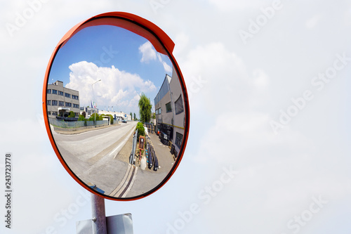 Outdoor convex safety mirror hanging on wall with reflection of an urban roadside view of cars parked along the street by residential apartment buildings. photo