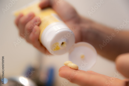 Young Caucasian Hands Squeezing Tube and Applying Acne Face Wash Lotion Skin Care Product Close Up and Zoomed In in Home Bathroom next to Sink and Mirror for Hygiene  Personal Care  and Cleanliness