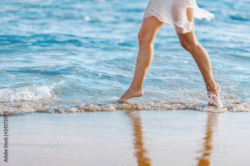 Beautiful young girl running on the beach barefoot in the water. Girl walking barefoot in the water at sunset.