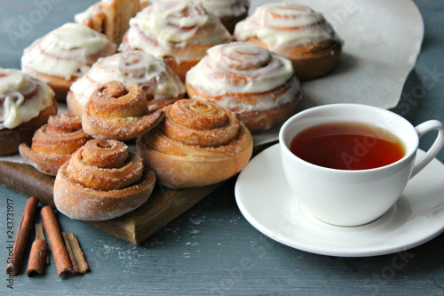  Cinnamon rolls and a Cup of tea on a wooden table. Fresh homemade nuns with cinnamon, a cup of tea, cinnamon sticks. Selective focus, close-up