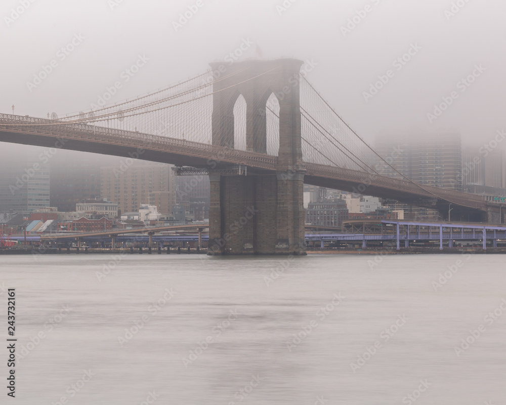View on Brooklyn Bridge from east river on a foggy day with long exposure
