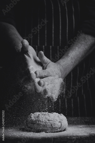 Flour is sprinkled over a ball of dough on a wooden board by hand in artistic conversion