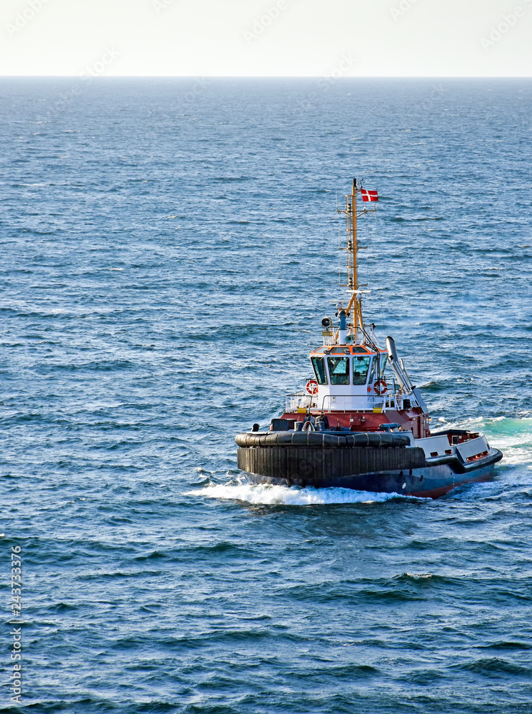 A tugboat with a Danish flag navigates on the sea A tugboat with a Danish flag navigates on the sea