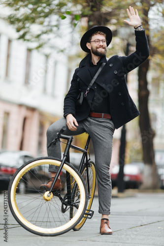 Handsome hipster man riding bike and waving Hello.