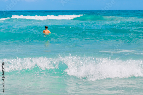 Young beautiful girl swimming in the blue waves of the Indian ocean. A girl stands waist-deep in water.