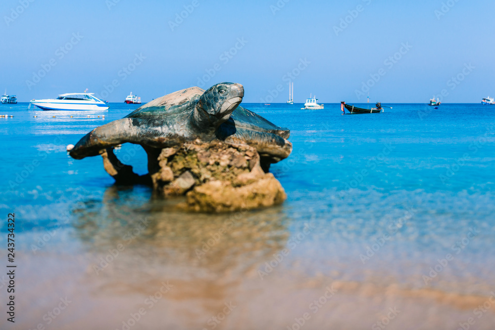 The sculpture of a turtle. The symbol of the island of Koh Tao. Turtle on the ocean background. Boats in the beautiful blue sea