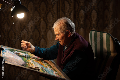 Elderly man woving a tapestry under bright light in living room on winter evening photo