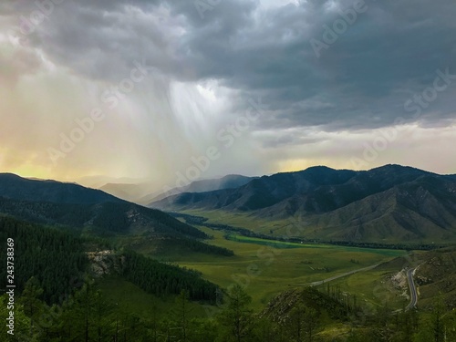 Summer landscape with mountains and river. Rain and clouds in the background. Top view of the green mountains.