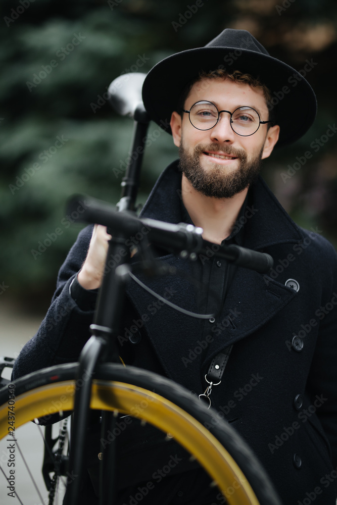 Bearded man with a fixie bicycle. Low angle view of confident young bearded man carrying his bicycle on shoulder and looking at camera while walking outdoors. Bearded man with a fixie bicycle. Low angle view of confident young bearded man carrying his bicycle on shoulder and looking at camera while walking outdoors.