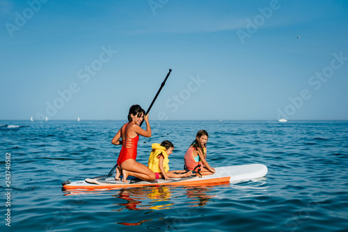 Mother with two daughters stand up on a paddle board photo