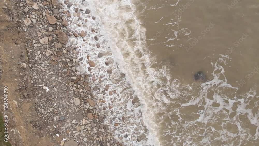 Aerial view of a surf of the dirty black sea with a rocky coast.