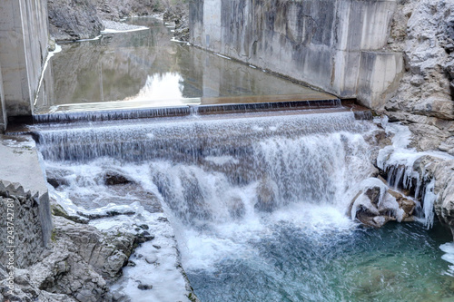 A small waterfall over concrete in the Veral river with grey rock and cold ice stalactites in the Foz de Binies zone, during winter, in Aragon, Spain photo