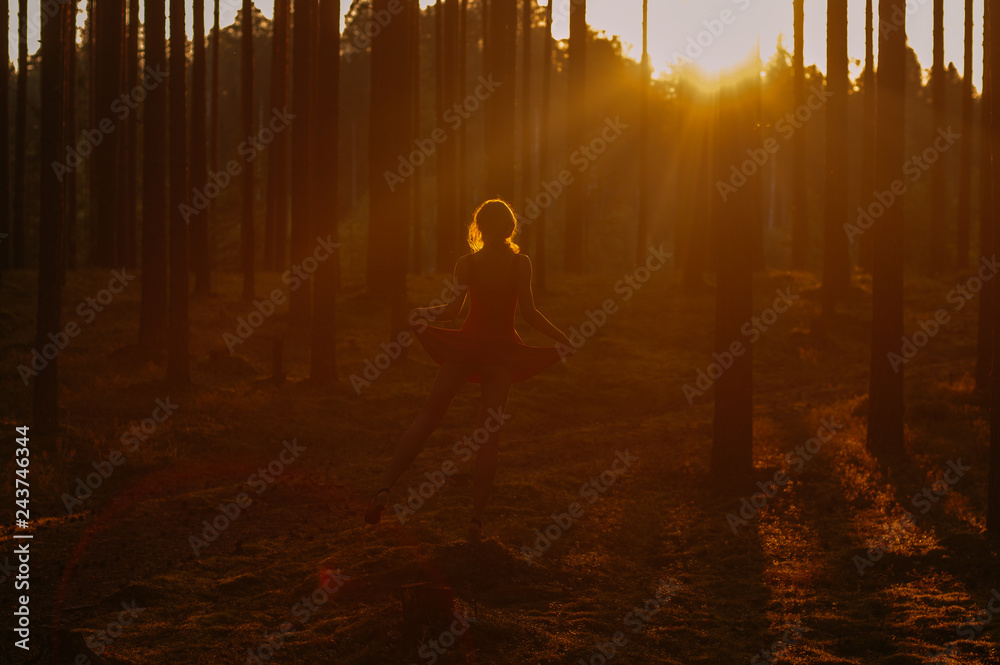 Young girl in red dress staying on one leg on the stump in forest Young girl in red dress staying on one leg on the stump in forest