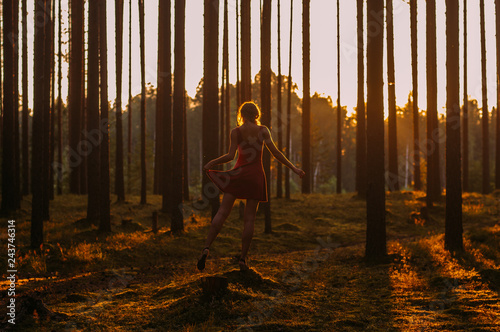 Young girl in red dress staying on the stump on one leg in forest